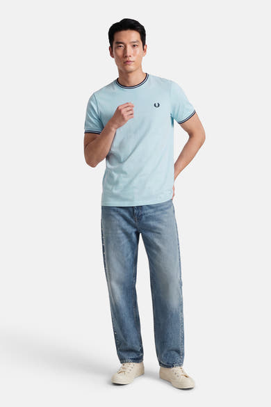T-shirt bleu clair à manches courtes de Fred Perry, avec col et manches contrastés, porté avec un jean bleu ample.