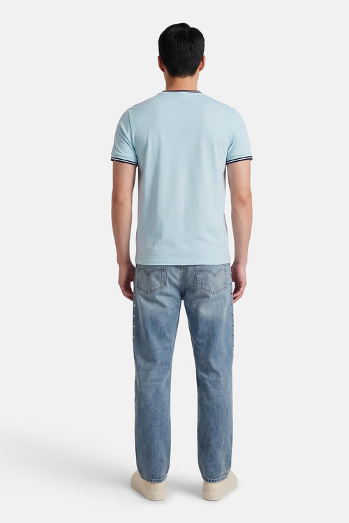 T-shirt bleu à manches courtes de FRED PERRY, avec détails rayés au col et aux manches, porté avec un jean.
