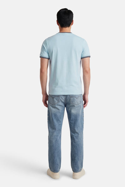 Blauw T-shirt met korte mouwen van FRED PERRY, met gestreepte details op de kraag en mouwen, gedragen met een spijkerbroek.