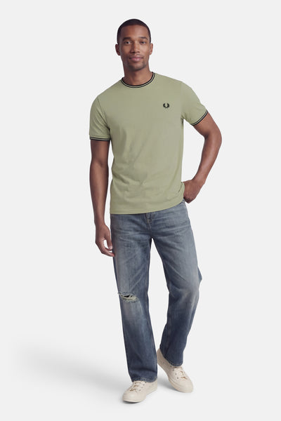 T-shirt vert à manches courtes de FRED PERRY, avec rayures noires au col et aux manches, porté avec un jean bleu