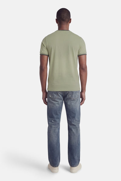 Groen T-shirt met korte mouwen van FRED PERRY, met gestreepte details op de kraag en mouwen, gedragen met een verbleekte spijkerbroek.