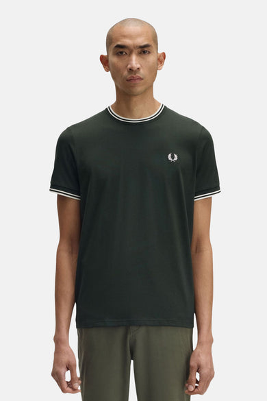 Groen T-shirt met korte mouwen van Fred Perry, met witte strepen op de kraag en mouwen, gedragen met een kaki broek.