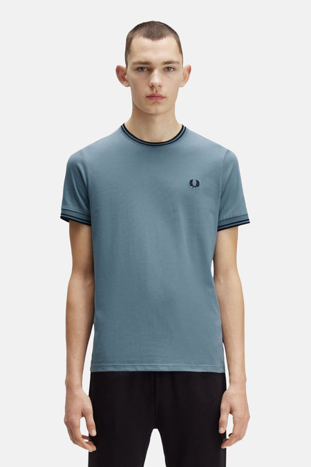 Blauw T-shirt met korte mouwen van FRED PERRY, gestreepte ronde hals, discreet logo op de borst, gedragen met een zwarte broek.