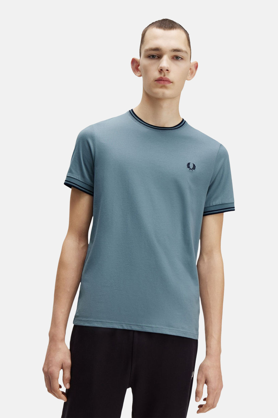 Blauw T-shirt met korte mouwen van FRED PERRY, met decoratieve strepen op de kraag en mouwen, gedragen met een zwarte broek.