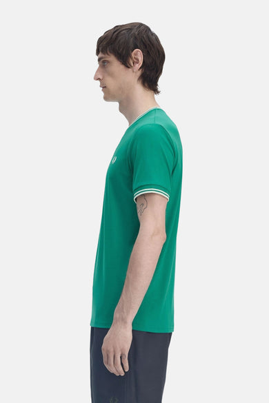 T-shirt met Fred Perry, groen, met korte mouwen en gestreepte kraag en mouwen, gedragen met een donkere broek.