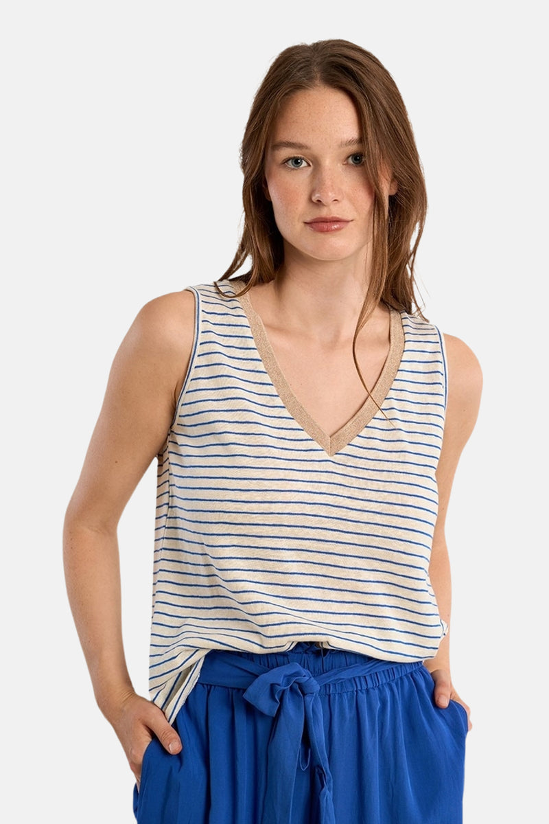 T-shirt écru à rayures bleues par Molly Bracken, avec un col en V doré, porté avec un pantalon bleu à taille nouée.