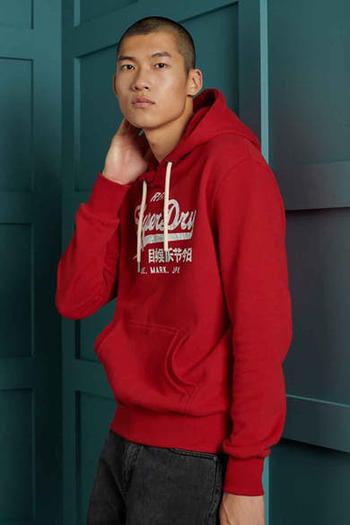 Rode SUPERDRY hoodie met witte trekkoord en kangoeroezak, gedragen met een zwarte jeans.
