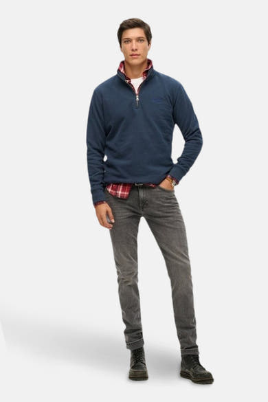 Marineblauwe sweatshirt met ritssluiting van SUPERDRY, gedragen over een rood geruit overhemd en grijze jeans.