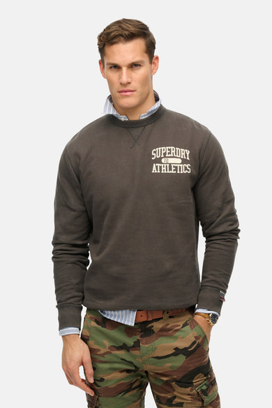 Sweat col rond gris de Superdry, porté sur une chemise rayée et un pantalon camouflage.
