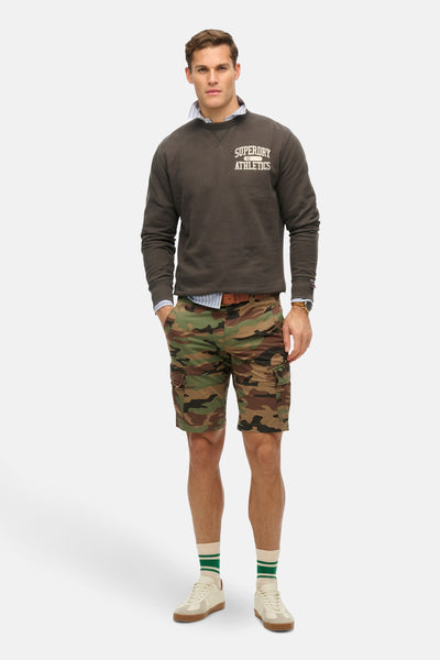 Sweat col rond gris de Superdry, porté avec une chemise rayée et un short camouflage.
