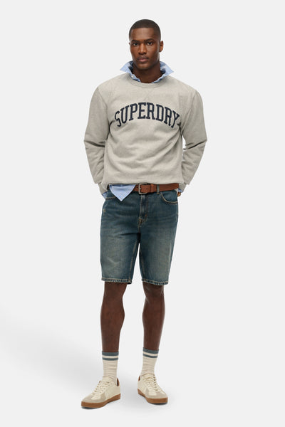 Sweat-shirt gris à col rond de SUPERDRY, porté avec une chemise, un short en jean et des baskets.
