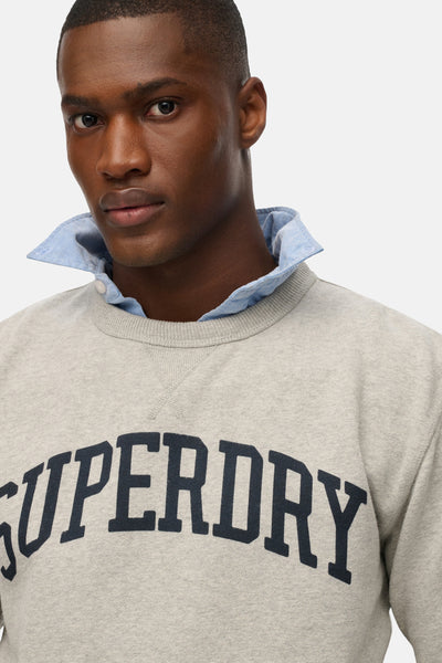 Sweat col rond gris de SUPERDRY avec logo sur le devant et col de chemise bleu clair visible.