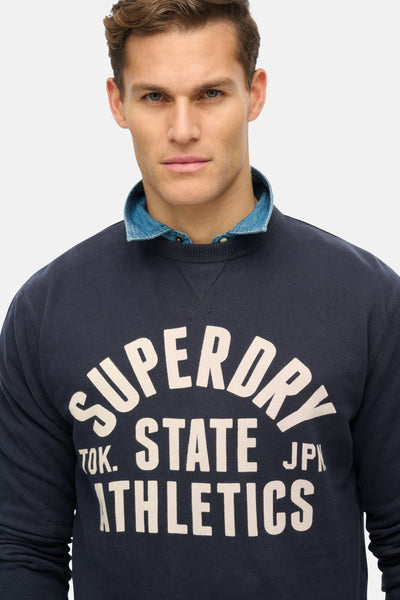 Sweat col rond bleu par Superdry, avec col chemise en jean et graphisme universitaire blanc.