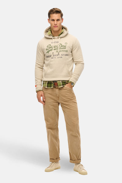 Beige hoodie van SUPERDRY, gedragen over een geruit overhemd, met een zandkleurige broek en sneakers.