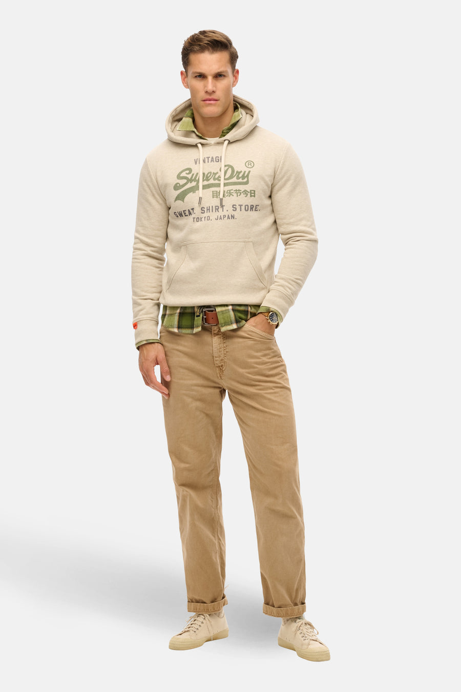 Beige hoodie van SUPERDRY, gedragen over een geruit overhemd, met een zandkleurige broek en sneakers.