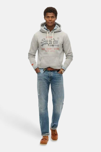 Grijze gebloemde Superdry hoodie, gedragen over een jeansblouse en een blauwe broek, metbrubruine schoenen.