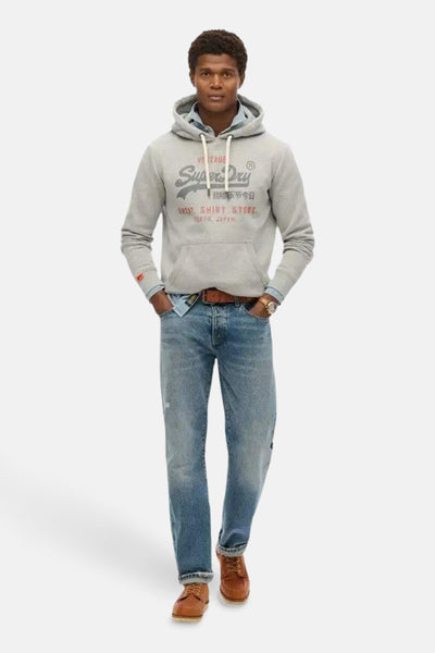 Grijze gebloemde Superdry hoodie, gedragen over een jeansblouse en een blauwe broek, metbrubruine schoenen.