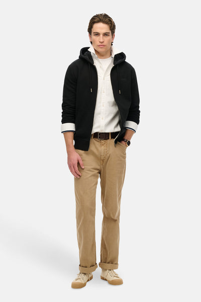 Gilet noir de Superdry, porté sur une chemise blanche avec pantalon chino beige et baskets.