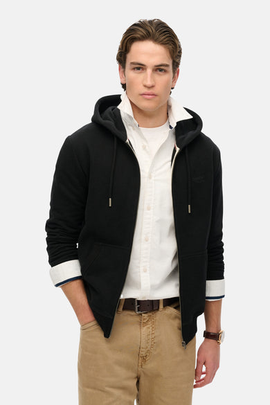 Gilet noir de SUPERDRY porté avec une chemise blanche et un pantalon chino beige.