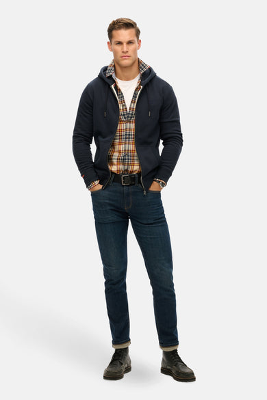 Donkerblauwe rits-sweatshirt van SUPERDRY gedragen over een geruit overhemd en een spijkerbroek.