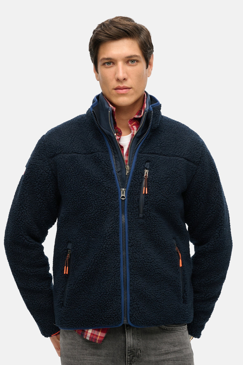 Blauwe SUPERDRY bodywarmer met ritssluiting, zakken met rits en rood geruite voering.