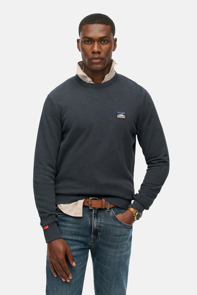 Marineblauwe trui van SUPERDRY, gedragen met een gebroken witte blouse, een spijkerbroek en een bruine riem.
