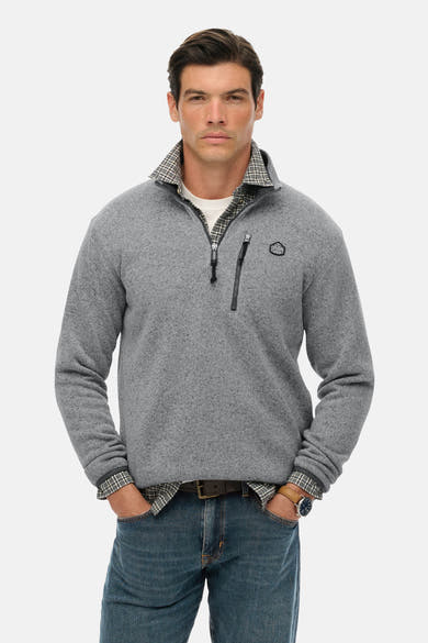 Grijze fleece van SUPERDRY, gedragen over een geruit overhemd, met ritssluiting tot halverwege en een blauwe spijkerbroek.