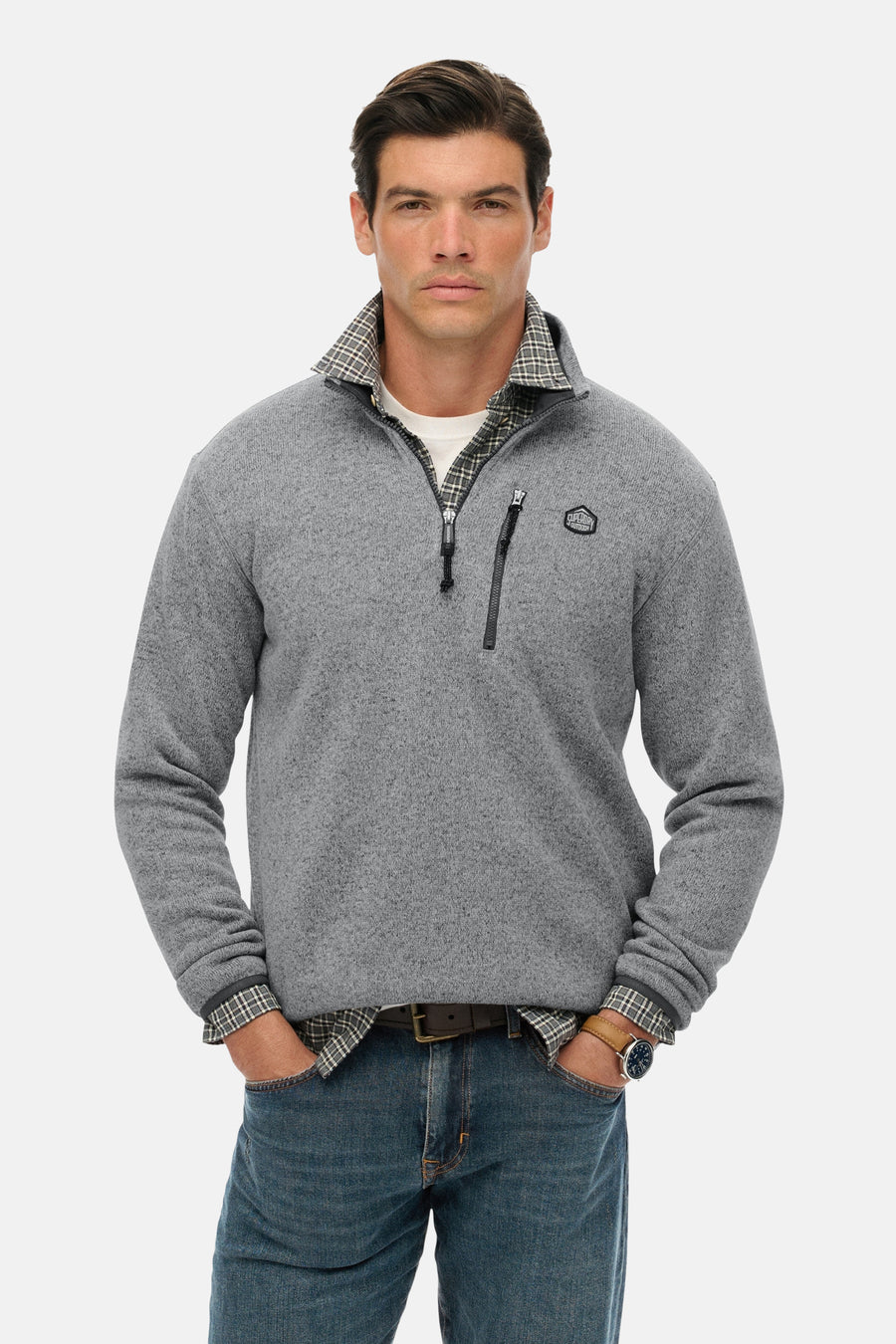 Grijze fleece van SUPERDRY, gedragen over een geruit overhemd, met ritssluiting tot halverwege en een blauwe spijkerbroek.
