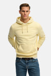 Sweat à capuche jaune de SUPERDRY, avec cordon de serrage, poche kangourou et porté sur un jean et une ceinture marron.
