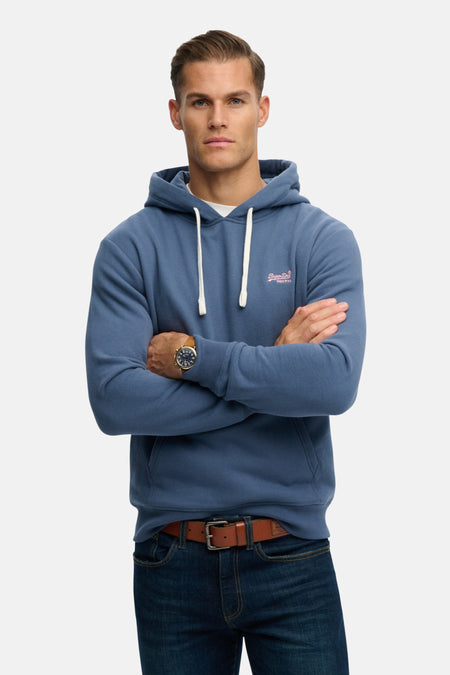 Sweat à capuche bleu de Superdry, porté par un homme, avec un jean et une ceinture marron.

