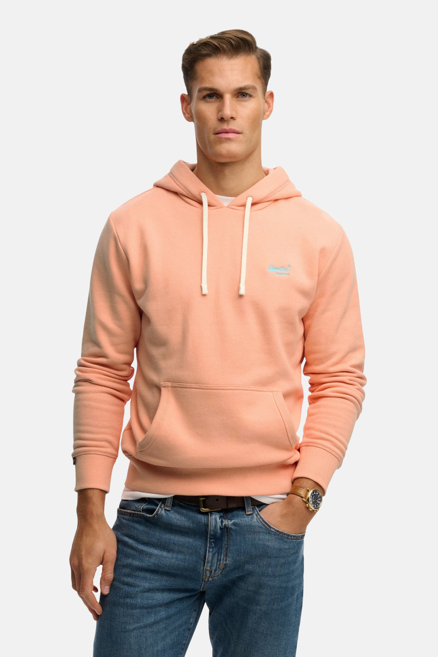 Sweat à capuche orange de SUPERDRY, avec cordon blanc et poche kangourou, porté avec un jean et une montre.
