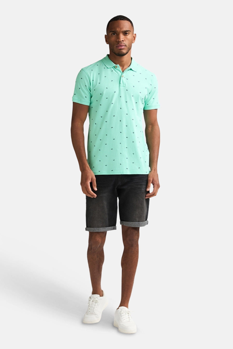 Groen poloshirt van Petrol Industries met een patroon van kleine ankers, gedragen met een zwarte spijkerbroek en witte sneakers.