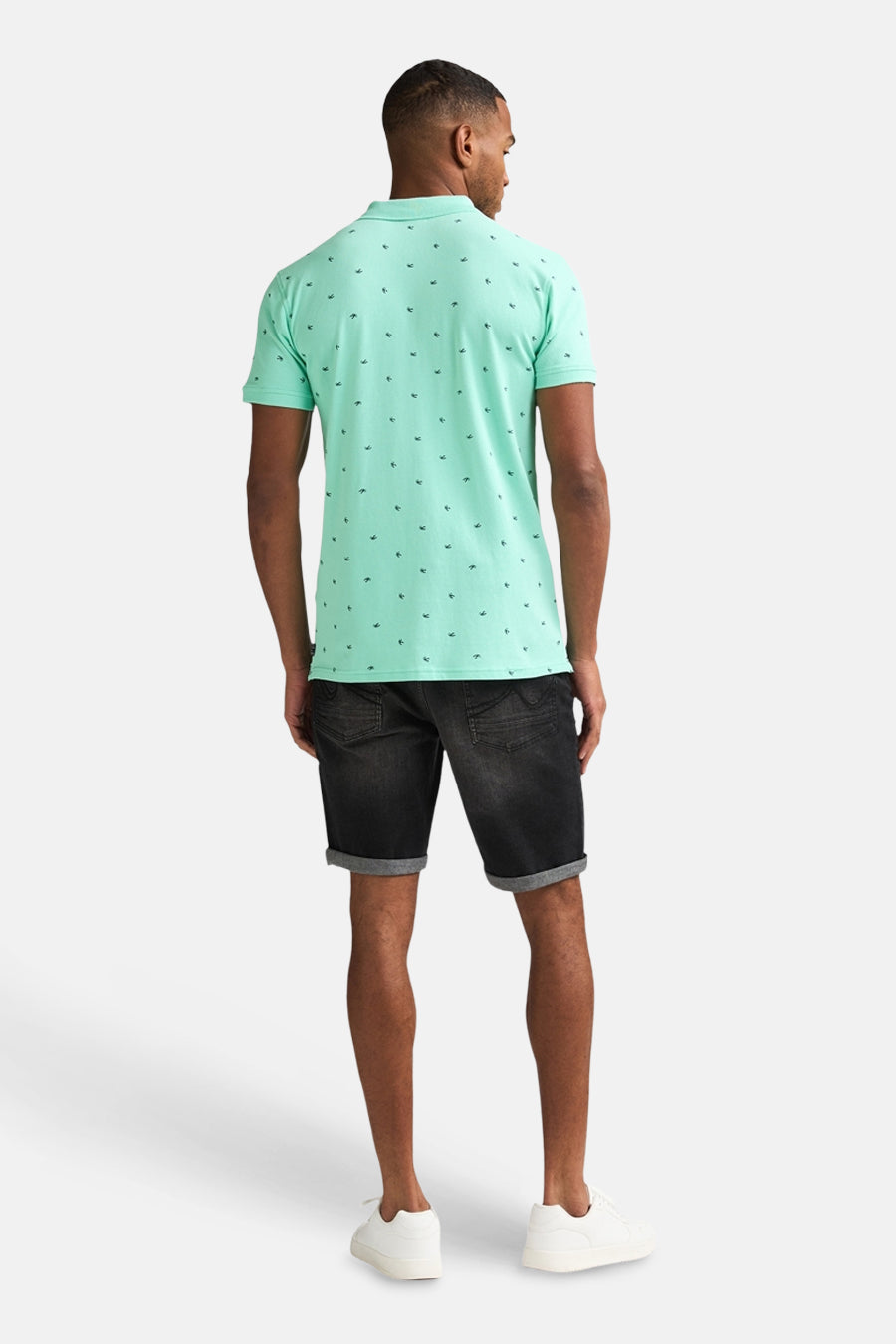 Polo vert de Petrol Industries à motif petits oiseaux, porté de dos avec un short en jean noir.