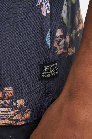 Polo multicolore de Petrol Industries avec motif floral abstrait sur tissu piqué bleu foncé et étiquette tissée noire latérale.