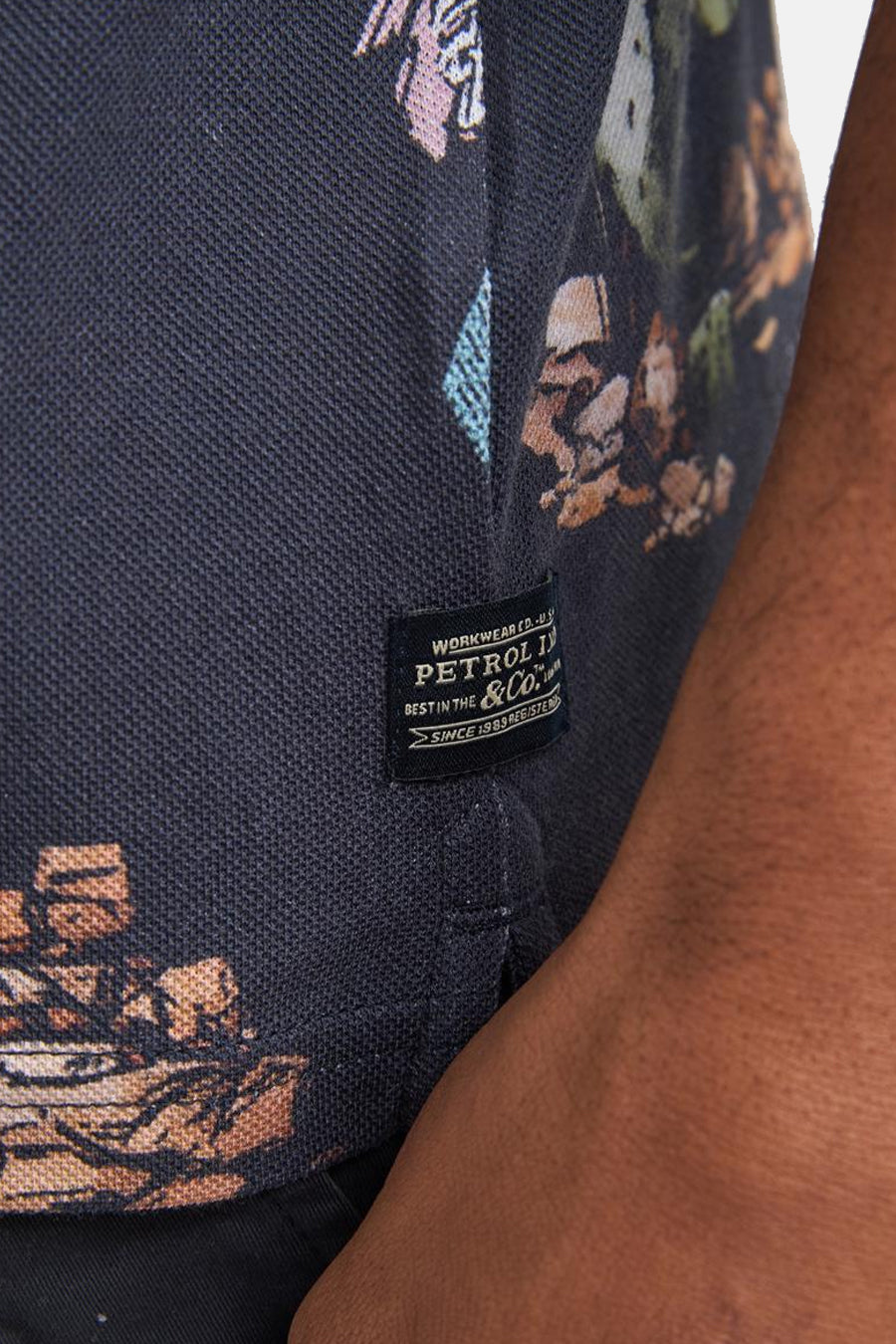 Polo multicolore de Petrol Industries avec motif floral abstrait sur tissu piqué bleu foncé et étiquette tissée noire latérale.