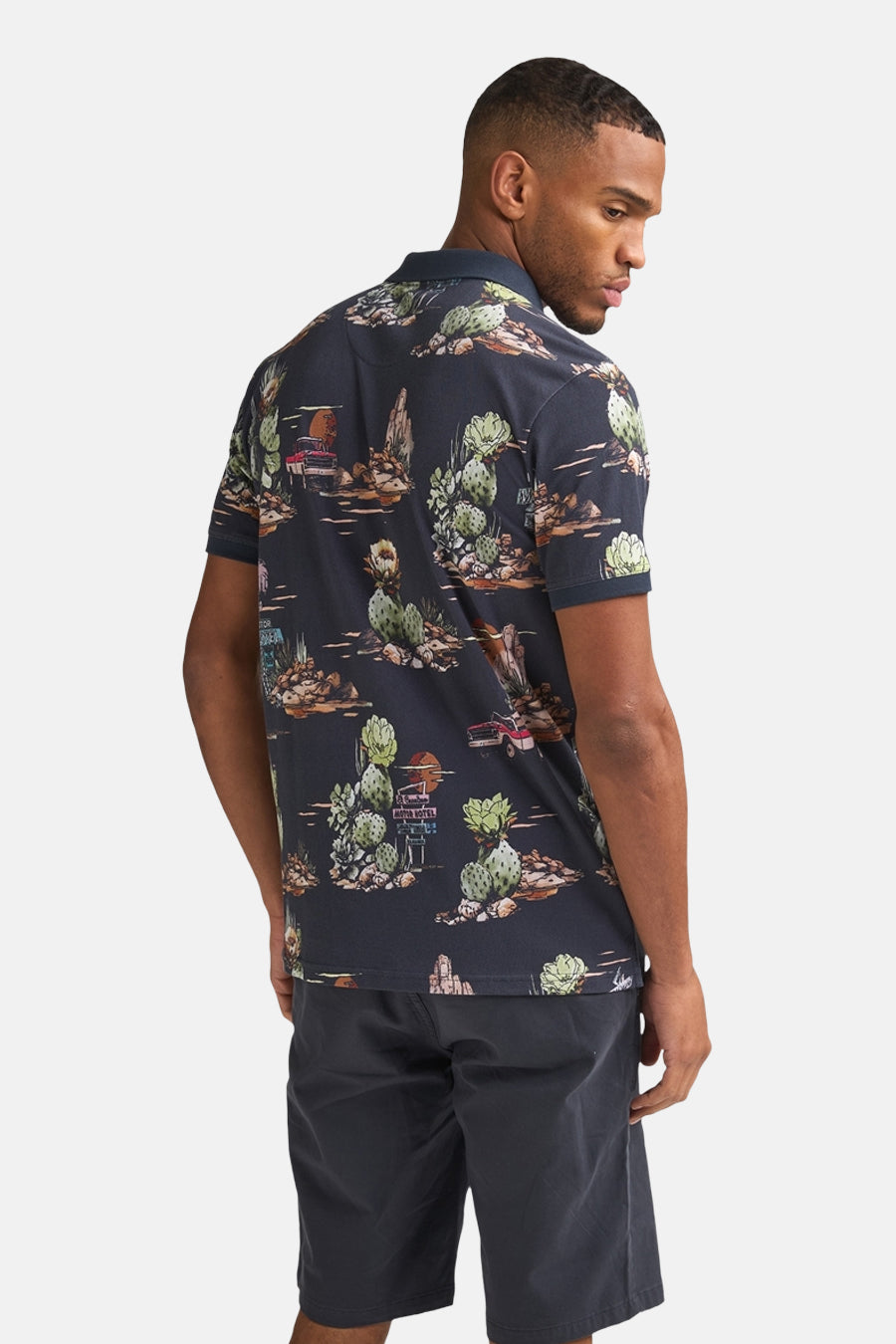 Multikleurig Petrol Industries poloshirt met woestijn- en cactusthema, van achteren gedragen met een donkere korte broek.