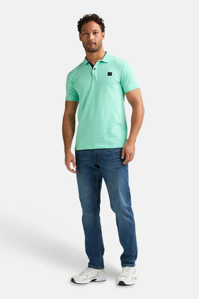 Groen poloshirt van Petrol Industries®, met een zwart embleem op de borst, gedragen met een spijkerbroek en sneakers.