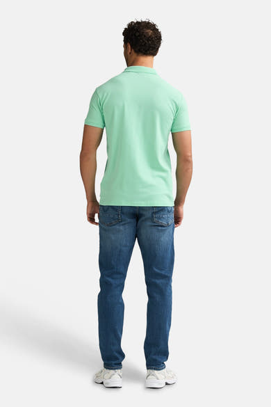 Polo vert par Petrol Industries®, vue de dos, porté avec un jean bleu et des baskets blanches.