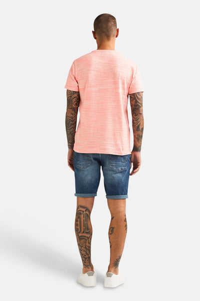 T-shirt corail par Petrol Industries®, porté avec un short en jean et des tatouages sur les bras et les jambes.