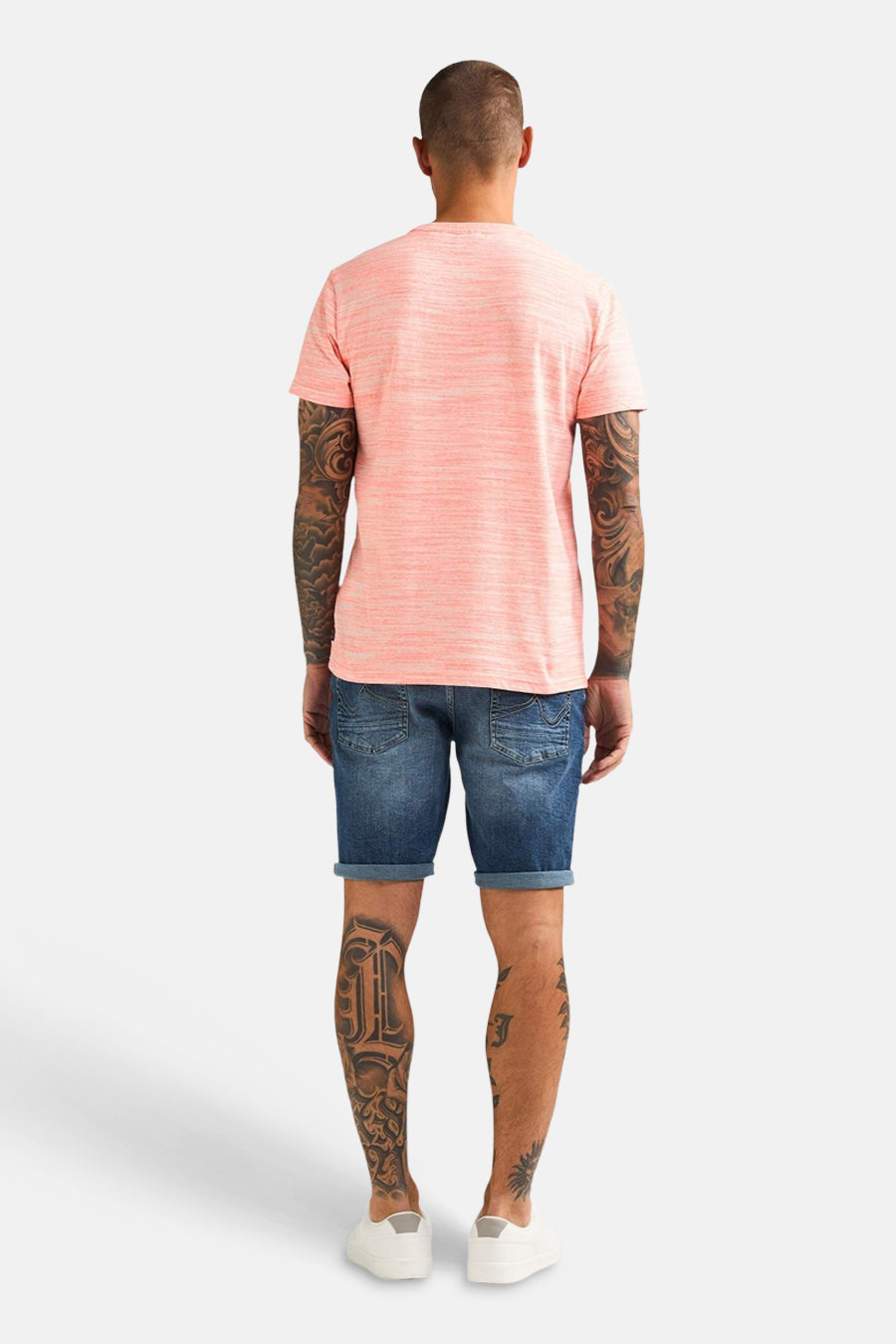 T-shirt corail par Petrol Industries®, porté avec un short en jean et des tatouages sur les bras et les jambes.