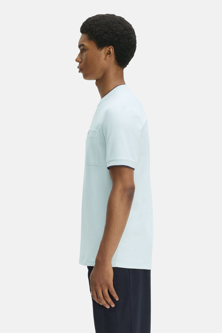 T-shirt bleu clair de FRED PERRY en maille piquée, avec col rond, poche poitrine et bordures foncées, porté de profil.