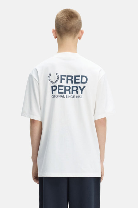 Wit Fred Perry T-shirt met groot marineblauw logo op de rug, gedragen door een man van achteren.