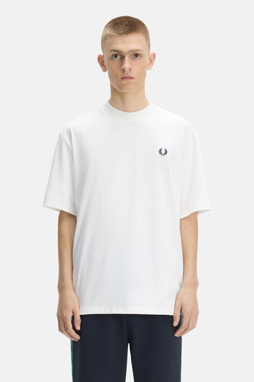 T-shirt blanc à manches courtes de Fred Perry avec un logo couronne de laurier bleu marine sur la poitrine, porté par un homme en vue de face.