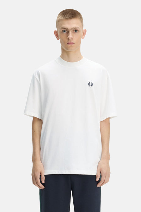 T-shirt blanc à manches courtes de Fred Perry avec un logo couronne de laurier bleu marine sur la poitrine, porté par un homme en vue de face.