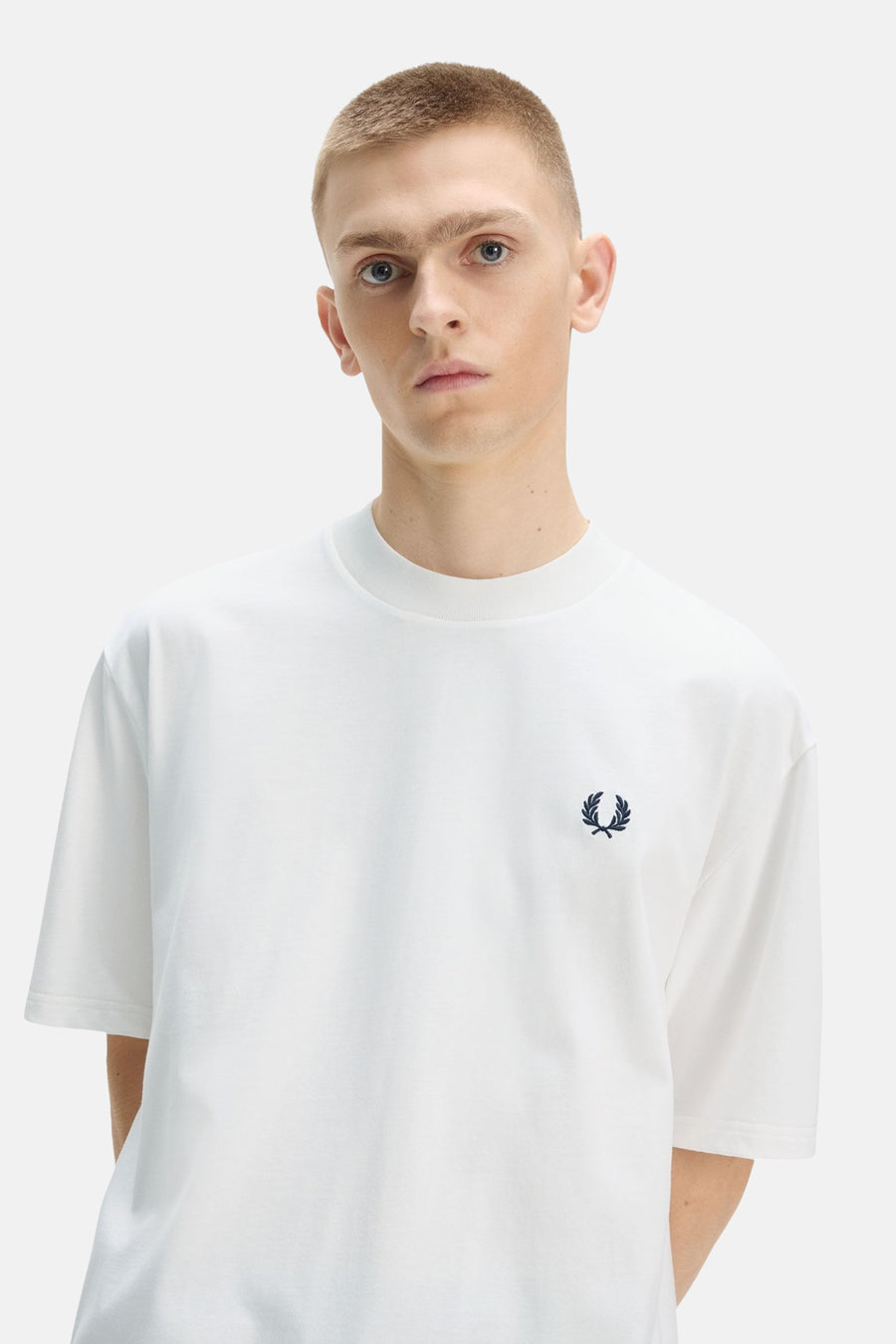 Wit T-shirt van FRED PERRY met ronde hals en marineblauw lauriertaklogo op de borst, gedragen door een man.