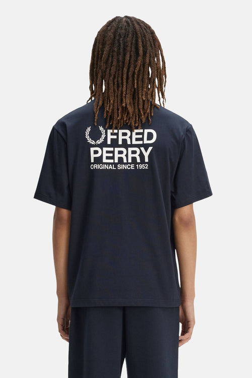 T-shirt bleu marine de FRED PERRY, dos avec logo laurier et texte blanc, porté avec un bas assorti.