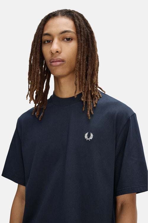 T-shirt bleu marine de FRED PERRY, avec le logo couronne de laurier blanc, porté par un homme aux dreadlocks.