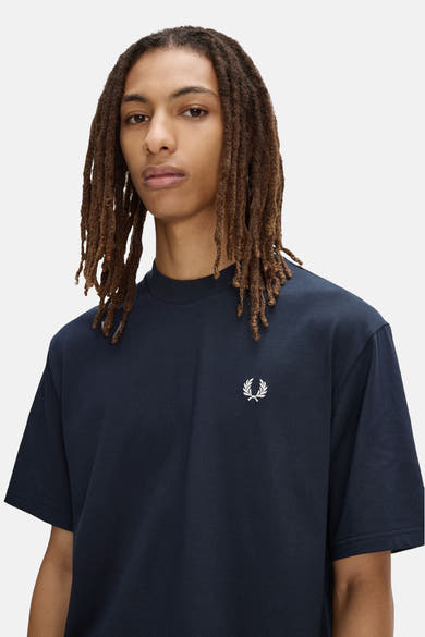 Marineblauwe T-shirt van FRED PERRY, met het witte lauriertaklogo, gedragen door een man met dreadlocks.
