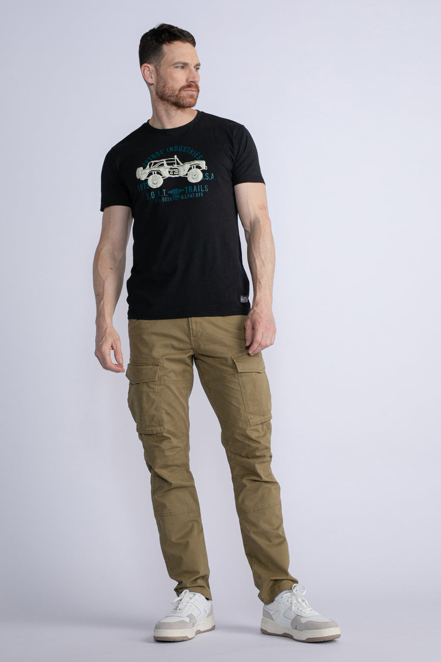 Groene cargobroek van Petrol Industries, gedragen met een zwart T-shirt met grafische print en witte sneakers.