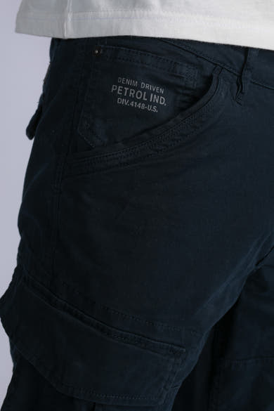Blauwe cargobroek van Petrol Industries, met klepzak en stikseldetails, gedragen met een wit T-shirt.